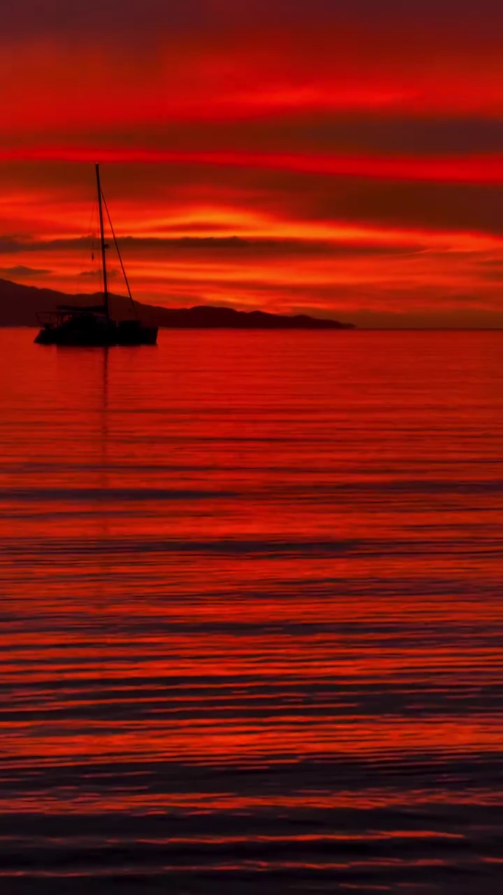 Tramonto rosso sul mare di Cagliari, con una barca a vela